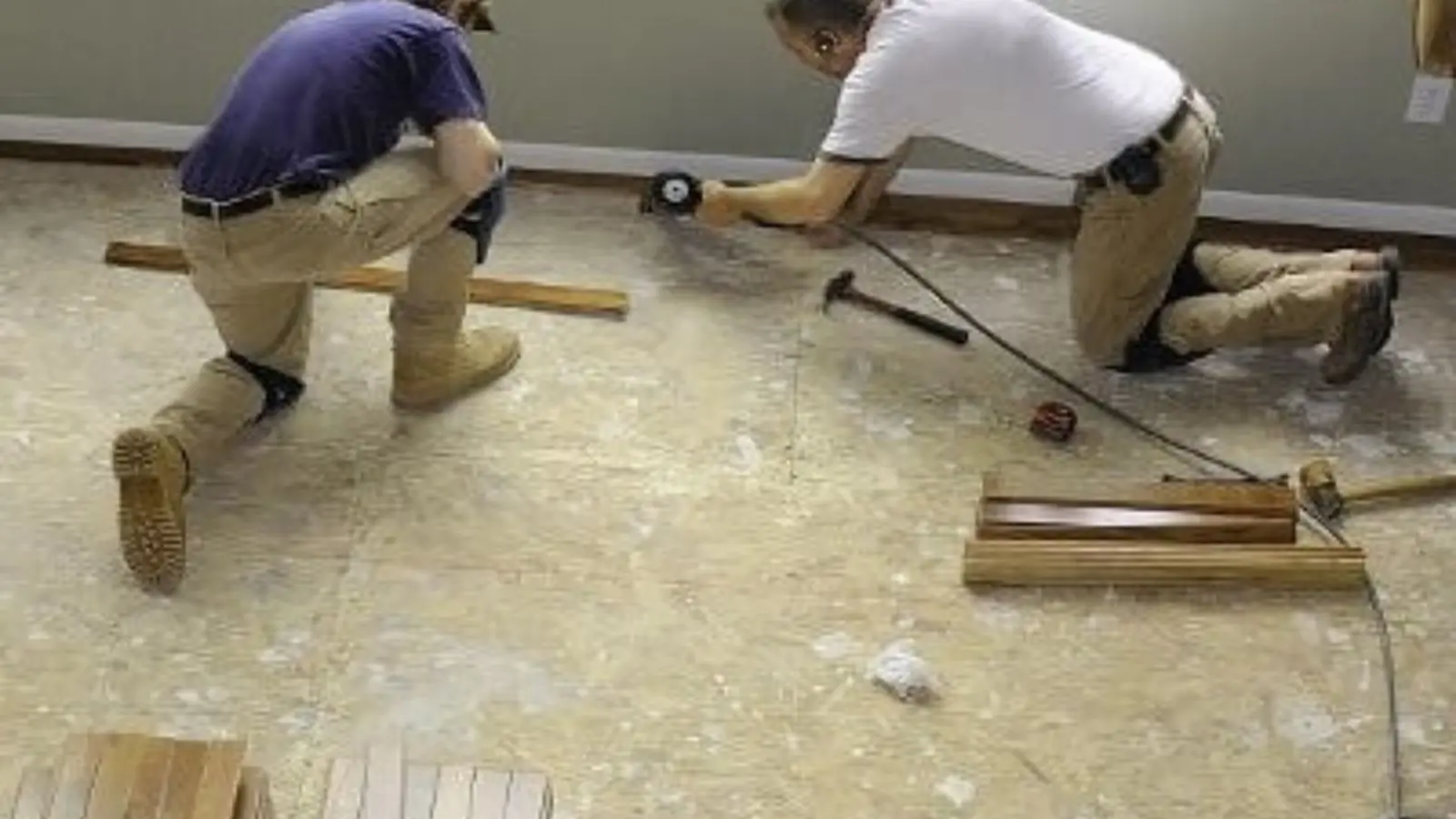 Two workers kneeling on a floor installing replacement flooring after water damage