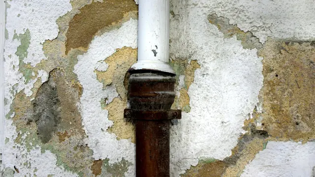 Peeling plaster and rust staining around a pipe on a water damaged wall